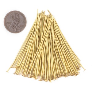 May include: A large pile of gold-coloured head pins with flat heads. The pins are approximately 2.5 cm long and are arranged in a fan shape.