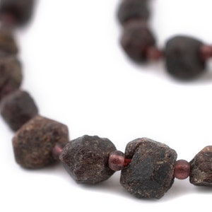 May include: A close-up of a necklace made of dark brown, faceted gemstone beads separated by small, shiny, copper-coloured beads.