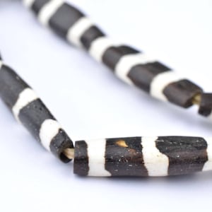 Puede incluir: Primer plano de un collar de rayas blancas y negras hecho de cuentas cilíndricas. Las cuentas están hechas de un material natural, posiblemente hueso o madera.