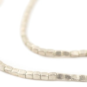 May include: Close-up of a silver necklace with small, square beads. The necklace is made of a metallic material and has a textured, matte finish. The beads are evenly spaced along the chain, creating a simple, elegant design.