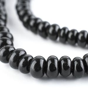 May include: Close-up of a black beaded necklace against a white background. The beads are smooth, glossy, and evenly sized, creating a simple yet elegant design. The necklace is likely for jewelry making or personal adornment.