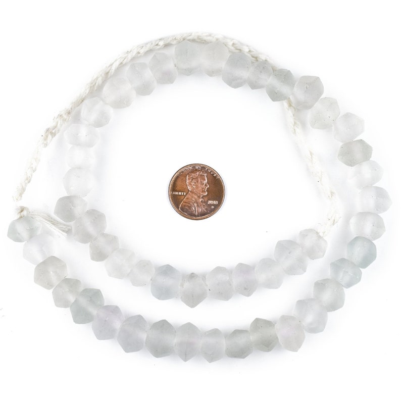May include: A strand of opaque white glass beads with a faceted, hexagonal shape. The beads are strung on a white cord and are approximately the size of a US penny.