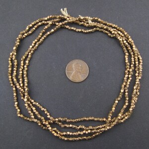 May include: A strand of gold-toned metal beads, each bead is faceted and shaped like a small pyramid. The beads are arranged in a circle and are about the size of a US penny.