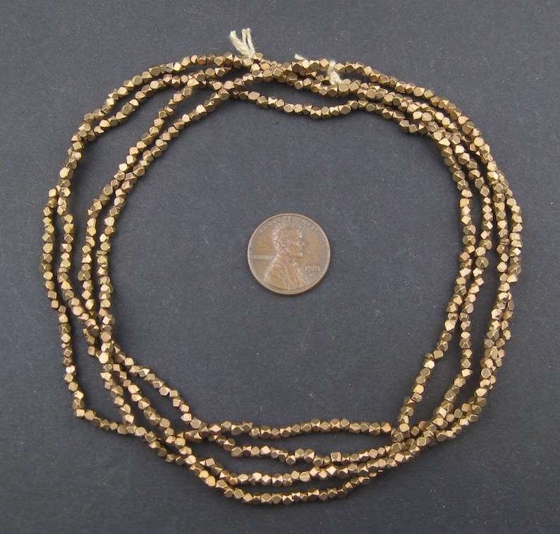 May include: A strand of gold-toned metal beads, each bead is faceted and shaped like a small pyramid. The beads are arranged in a circle and are about the size of a US penny.