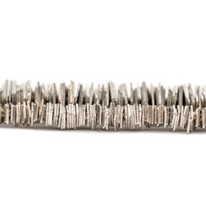 Puede incluir: Primer plano de una cadena de metal plateado hecha de pequeños eslabones rectangulares. La cadena está tendida sobre una superficie blanca.