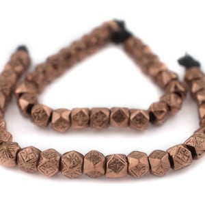 May include: A strand of copper-colored beads with a geometric design. The beads are strung on a black cord and are arranged in a circular shape.