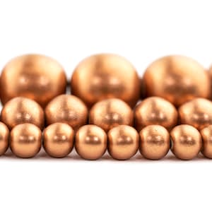 May include: A close-up of a row of copper-coloured beads. The beads are round and smooth, and they are arranged in a staggered pattern.