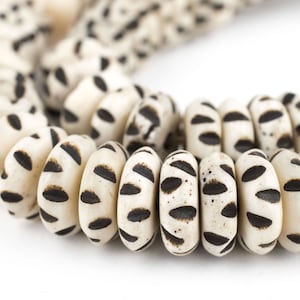 May include: A close-up of a white and black patterned necklace made of round beads. The beads are made of a natural material and have a slightly rough texture.