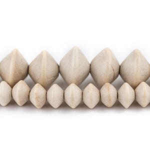May include: A strand of wooden beads in a light beige colour. The beads are faceted and have a diamond shape. The beads are arranged in a row, with the larger beads at the back and the smaller beads at the front.
