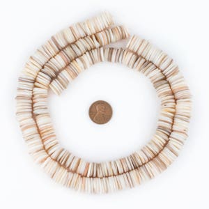 May include: A necklace of flat, round, off-white and tan shell beads arranged in a circular pattern. A U.S. penny is in the center for size comparison. The beads have a natural, organic appearance, with variations in color and texture.