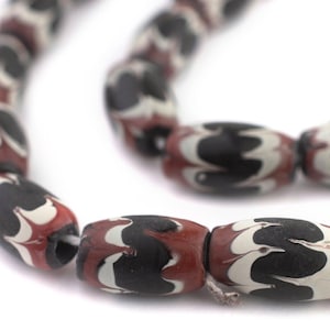 Könnte beinhalten: Nahaufnahme eines Strangs ovaler Perlen. Die Perlen sind hauptsächlich schwarz mit weißen und roten Wirbelmustern. Die Perlen sind aufgefädelt und bilden eine Halskette oder ein Armband.