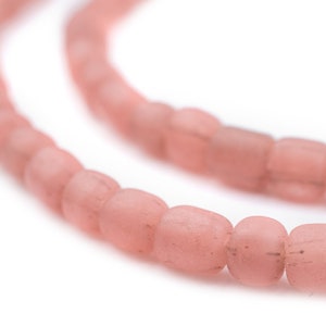 以下が含まれることがあります： 淡いピンク色の長方形のビーズの連なりのクローズアップ。ビーズはわずかにすりガラスのような外観で、白い背景に対して曲線を描いています。ビーズの長さは約1.3cmです。