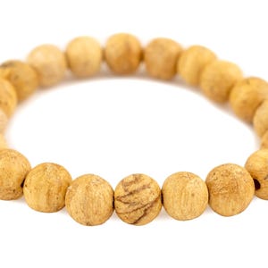 May include: A beaded bracelet composed of round, light brown beads. The beads have a natural, textured appearance, with variations in color and subtle patterns. The bracelet is displayed against a white background, highlighting the details of the beads.