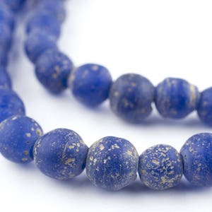 May include: A strand of blue glass beads with a speckled, aged look. The beads are round and have a matte finish.