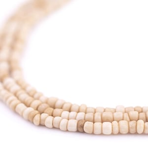 Könnte beinhalten: Nahaufnahme einer Schnur mit cremefarbenen Perlen. Die Perlen sind rund und glatt und auf einer dünnen Schnur aufgefädelt.