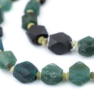 May include: A necklace made of faceted green and black glass beads. The beads are strung on a clear thread and have a slightly irregular shape.