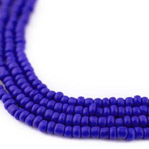 May include: Close-up of several strands of small, round, cobalt blue beads. The beads are tightly strung together, creating a textured, curved line against a white background. The beads appear to be made of glass or a similar material.