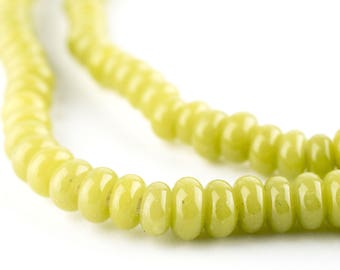 May include: Close-up of a strand of light green beads. The beads are oval-shaped and have a glossy finish. The beads are strung together, creating a necklace or bracelet. The background is white.