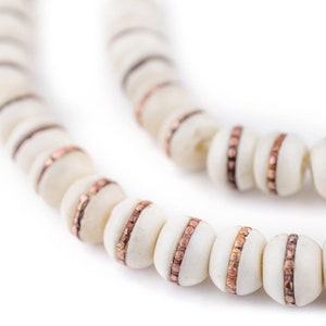 Può includere: Una collana di perle bianche con accenti in rame. Le perle sono rotonde e hanno una finitura liscia e lucida. Gli accenti in rame sono sottili e delicati, aggiungendo un tocco di eleganza alla collana.
