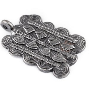 May include: A silver pendant with a detailed geometric design. The pendant has a loop at the top for attaching to a chain.
