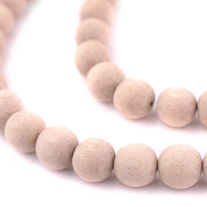 May include: Close-up of a strand of light beige wooden beads. The beads are round and have a natural wood grain pattern. The beads are strung together, creating a curved line against a white background. Ideal for jewelry making.