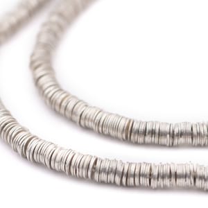Peut inclure: Un collier en argent composé de petites perles rondes et plates. Les perles sont enfilées les unes aux autres pour former une longue chaîne continue.