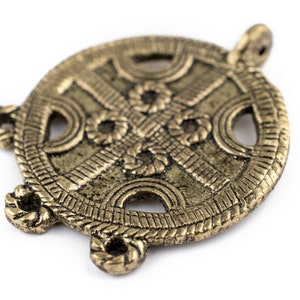 Peut inclure: Un pendentif circulaire de couleur bronze avec un motif de nœud celtique complexe. Le pendentif présente un motif de croix central, entouré d'un bordure en forme de corde et d'éléments décoratifs. Il possède quatre boucles d'attache.