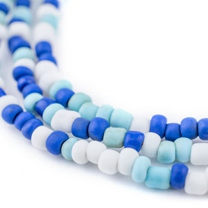 May include: Close-up of three strands of beaded necklaces. The beads are in shades of blue, white, and turquoise. The beads are small and round, and the necklaces are arranged in a curved pattern against a white background.