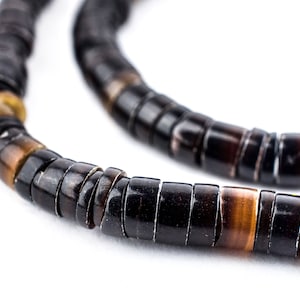 Könnte beinhalten: Nahaufnahme einer Halskette aus schwarzen und braunen Muschelkugeln. Die Kugeln sind rund und haben eine glatte, polierte Oberfläche.
