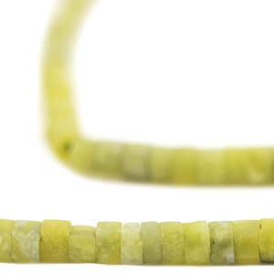 May include: A necklace composed of small, square-shaped beads in shades of pale yellow and green. The beads are strung together, creating a continuous loop. The background is plain white, highlighting the necklace's color and texture.