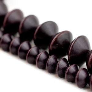 Puede incluir: Una hebra de cuentas de madera marr&oacute;n oscuro con forma redondeada y ligeramente puntiaguda.