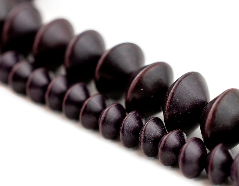 Puede incluir: Una hebra de cuentas de madera marr&oacute;n oscuro con forma redondeada y ligeramente puntiaguda.