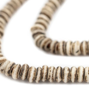 May include: A white and brown beaded necklace made from natural materials. The beads are round and have a slightly irregular shape. The necklace is strung on a thin cord.