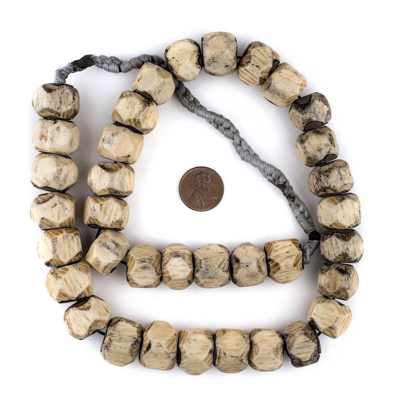 May include: A string of light brown wooden beads with a grey cord. The beads are faceted and have a worn, rustic look. The string of beads is about 50 cm long.