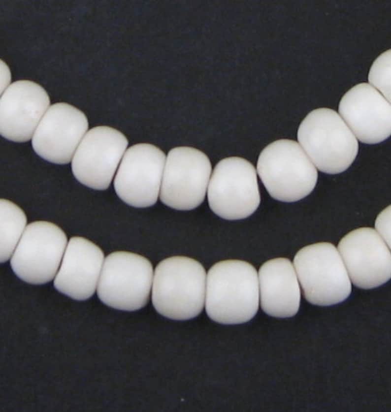 May include: Close-up of two strands of off-white, rounded beads against a dark background. The beads are evenly spaced and have a smooth, matte finish. The beads appear to be strung together, creating a necklace or bracelet.
