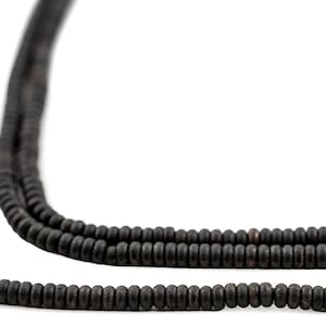 Puede incluir: Una hebra de cuentas de madera negra, con un acabado liso y mate. Las cuentas son redondas y de tamaño uniforme, creando un aspecto simple y elegante.