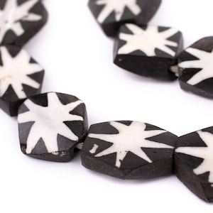 May include: A close-up of a black and white beaded necklace. The beads are shaped like stars and have a white star design on a black background.