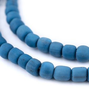 Puede incluir: Una hebra de cuentas de vidrio azul, cada cuenta es redonda y ligeramente alargada. Las cuentas están dispuestas en un patrón circular, creando un diseño simple y elegante.