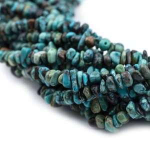 May include: A strand of turquoise chip beads, featuring a mix of blue and green hues with black matrix inclusions. The beads are irregular in shape and size, creating a natural and rustic look.