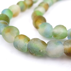 Peut inclure: Un brin de perles en verre vert, bleu et brun. Les perles sont de forme irrégulière et ont une finition givrée.