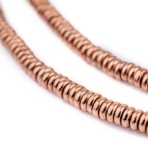 May include: A strand of copper-colored beads, each bead is a small, flat circle. The beads are strung together in a continuous line.