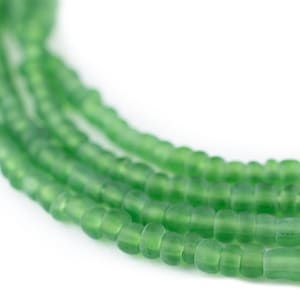 May include: Close-up of several strands of green glass beads. The beads are small, rectangular, and have a frosted appearance. The strands are arranged in a slightly curved pattern against a white background.