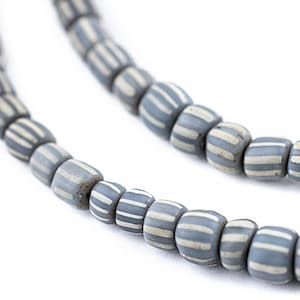 May include: A strand of gray and white striped glass beads. The beads are cylindrical and have a matte finish.