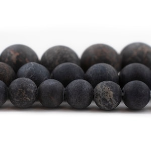 May include: Close-up of a strand of matte black beads. The beads are round with a slightly textured surface and varying shades of black and gray. The beads are strung together, creating a line of dark, spherical shapes.