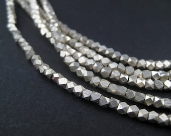 May include: A strand of silver-toned beads with a faceted, geometric shape. The beads are strung together to create a necklace or bracelet.