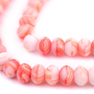 May include: A strand of pink and white shell beads with a swirling pattern. The beads are round and smooth.