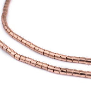 May include: A strand of rose gold colored metal beads. The beads are small and cylindrical in shape.