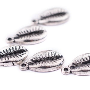 May include: Five silver cowrie shell charms with a textured surface. The charms have a hole at the top for attaching to jewelry or other crafts.