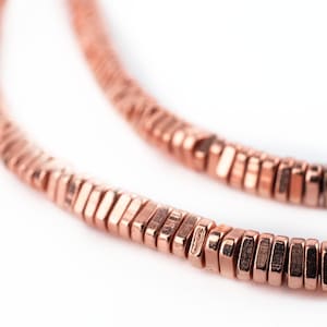 May include: A close-up of a rose gold necklace made of small, flat, hexagonal beads.
