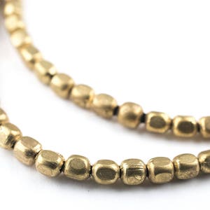 May include: A gold necklace made of small, square-shaped beads. The beads are strung on a black cord.